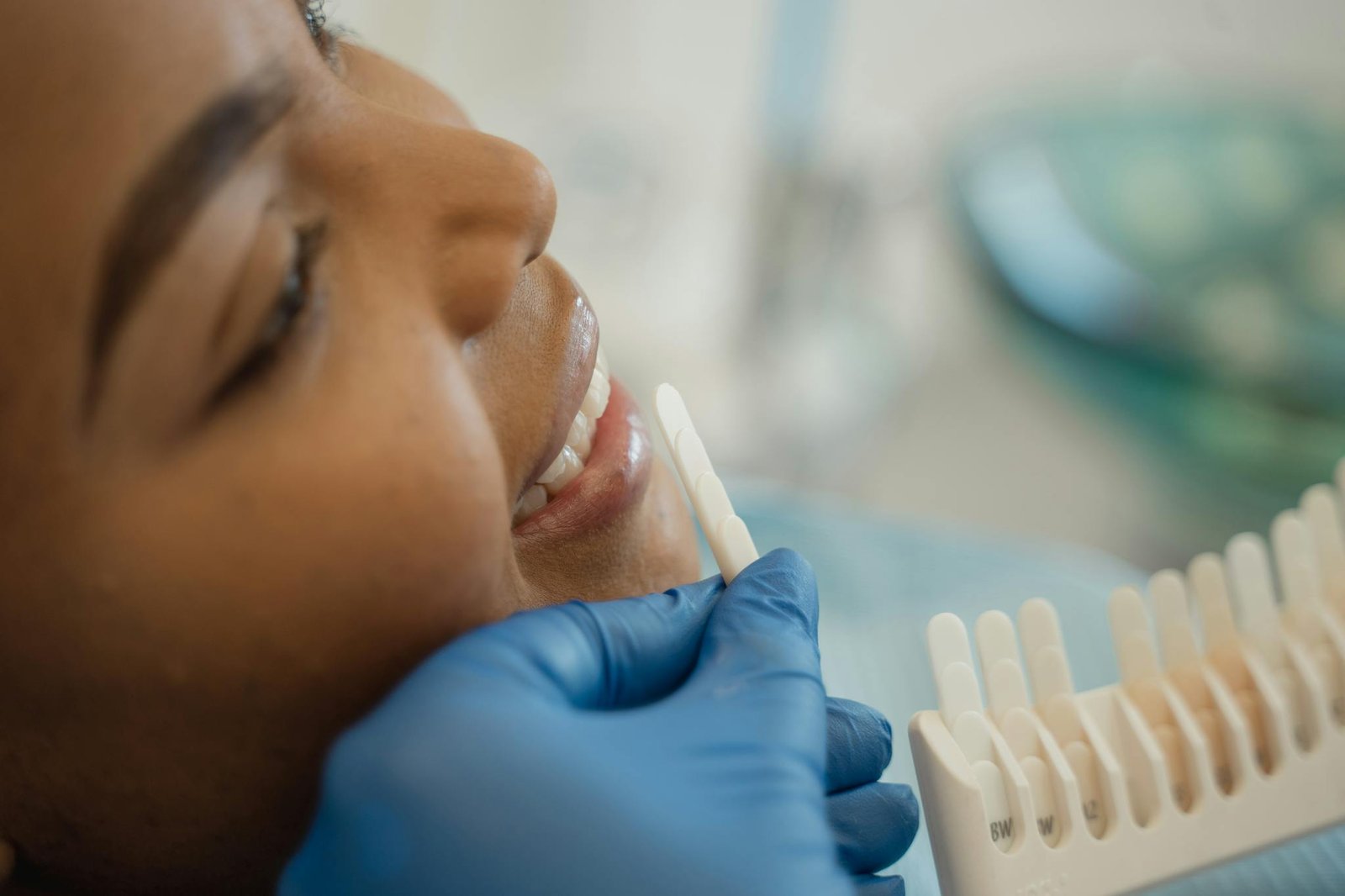 Smiling woman receiving a dental checkup with shade guide in the clinic.